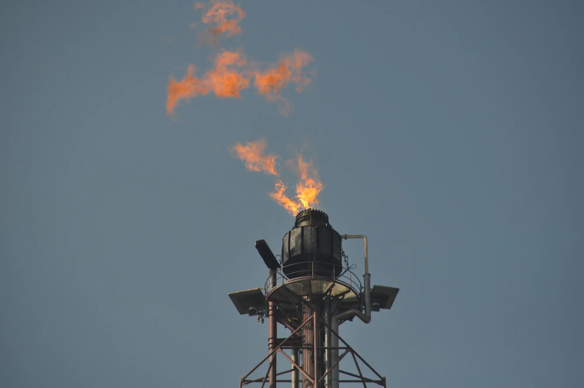 A gas flare stack burning against a grey sky